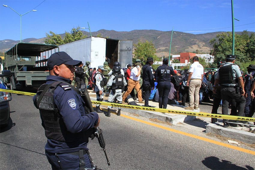 A state police officer stands guard as soldiers, National Guard members and other security agents begin to apprehend the migrants found in the trailer.