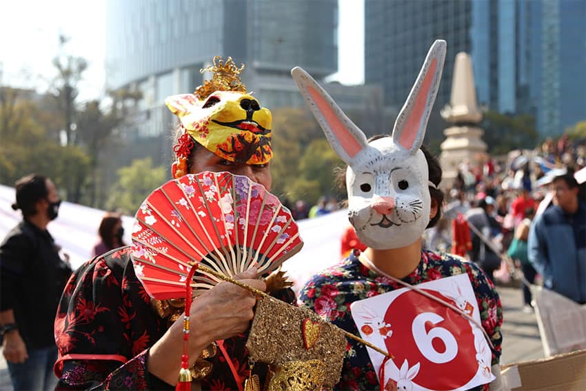 Two people with elaborate hand-made rabbit masks, fans and other accessories in a crowded urban setting.