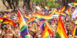 A outdoor crowd waving dozens of rainbow flags.
