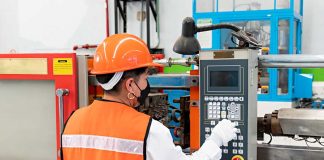 A woman in an orange vest and hard hat operates a machine in a factory