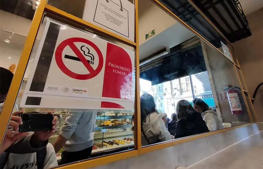 A no smoking sign on a mirrored wall in a pastry shop.