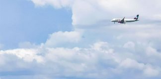 A Volaris airplane flies over palm trees with mountains in the background on a partly cloudy day.