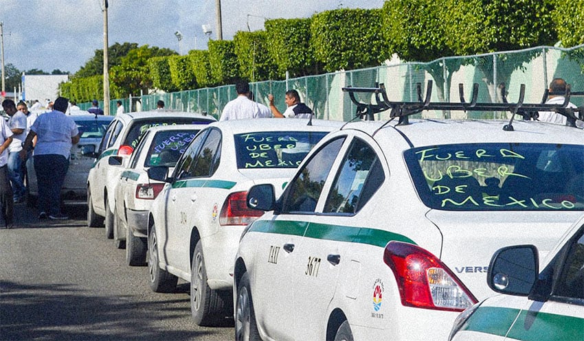 A line of taxis with "Fuera Uber de Mexico" written on the windows.