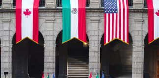 Enormous Canadian, Mexican and U.S. flags hang from stone archways in the National Palace in Mexico City, which the presidents of each country standing at small podiums far beneath each flag.