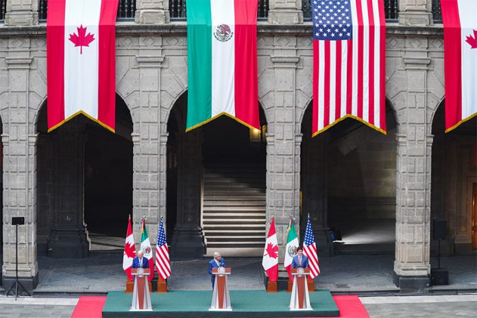 Enormous Canadian, Mexican and U.S. flags hang from stone archways in the National Palace in Mexico City, which the presidents of each country standing at small podiums far beneath each flag.