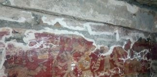 A mural painted on a wall, with human figures and symbols and a red background.