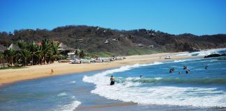 Two people sit on the beach in San Agustinillo, Oaxaca as others bathe in the surf.