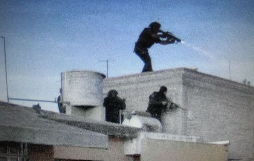 Zetas in military gear take cover behind a building