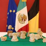 Archaeological pieces on a table in front of the EU, Mexican, and Belgian flags.