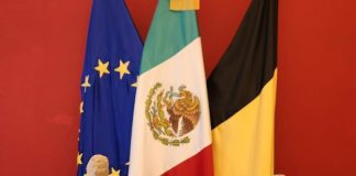 Archaeological pieces on a table in front of the EU, Mexican, and Belgian flags.