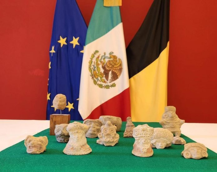 Archaeological pieces on a table in front of the EU, Mexican, and Belgian flags.