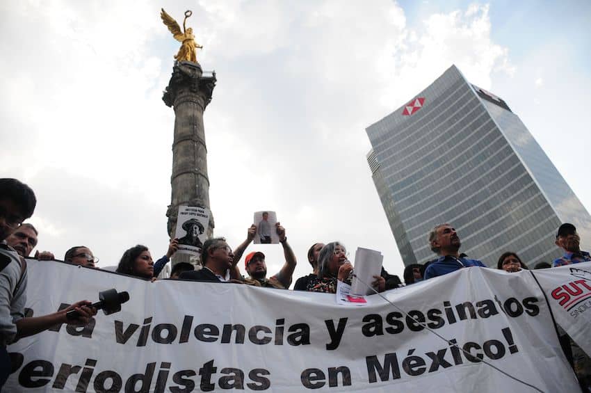Protesters hold banners and signs in front of Mexico City's Angel of Independence