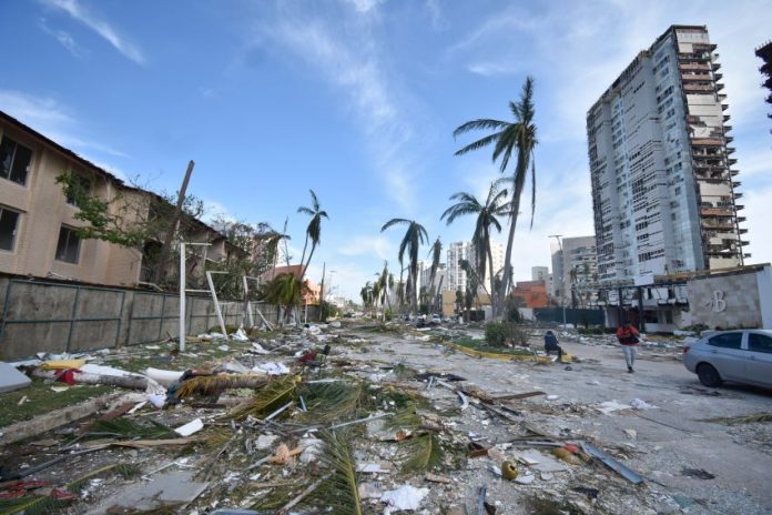 Pieces of debris litter a street lined with damaged palm trees and hotels.