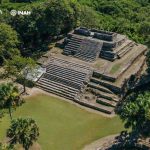 A stone pyramid rises out of a densely forested area.