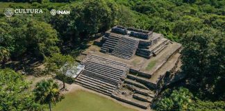 A stone pyramid rises out of a densely forested area.