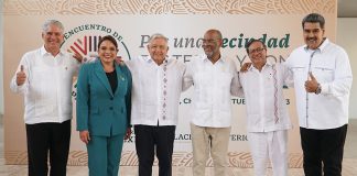 Six older men in white shirts and a woman in a green suit pose for a picture