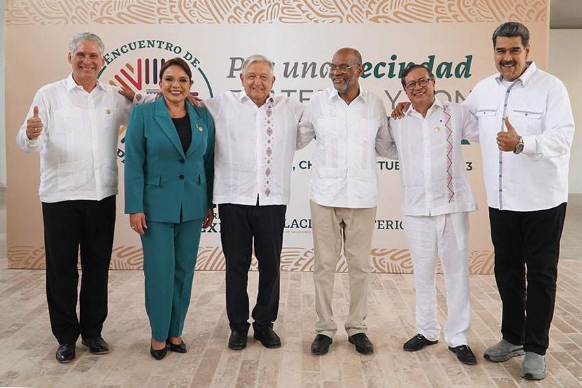 Six older men in white shirts and a woman in a green suit pose for a picture
