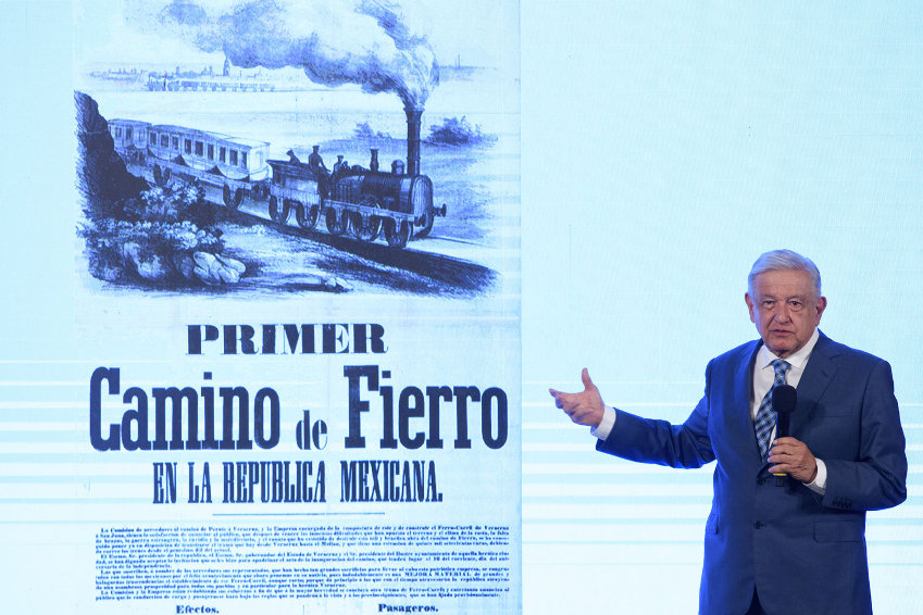 President L{opez Obrador gestures at a screen behind him, showing an historic train illustration