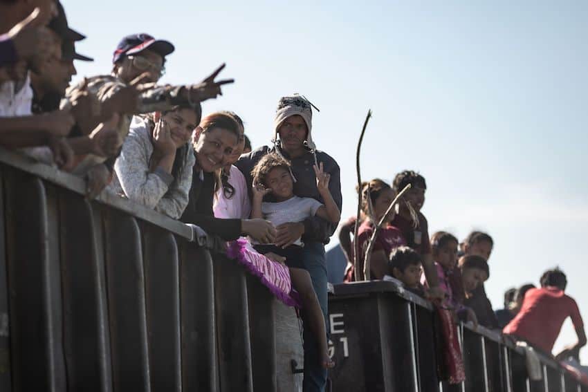 Men, women and children wave to the camera from atop the cars of a freight train.