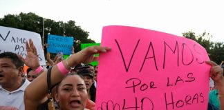 A woman holds a pink sign with the words "Vamos por las 40 horas" at a protest