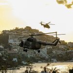 Two helicopters fly over the coast of Acapulco at twilight.