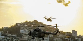 Two helicopters fly over the coast of Acapulco at twilight.