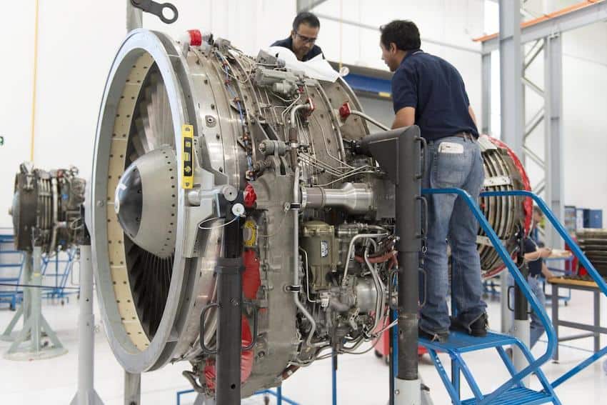 Two men on step ladders work on an airplane turbine, apparently building it