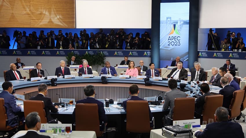 Roughly 20 national leaders sit at a large round table with screens behind them.