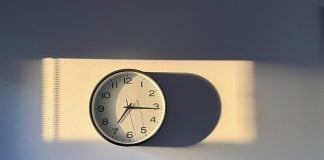 A clock casts a long shadow on a white wall.