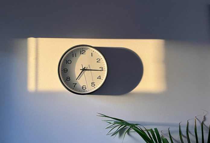 A clock casts a long shadow on a white wall.