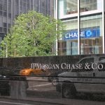 A stone sign reading JPMorgan & Chase Co. in front of a tree and tall buildings