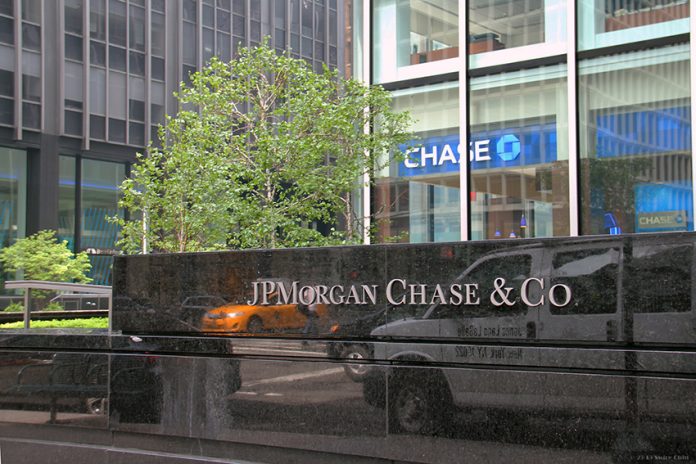 A stone sign reading JPMorgan & Chase Co. in front of a tree and tall buildings