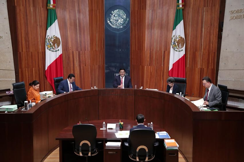 A courtroom with Mexican flags and 5 magistrates seated at the bench.