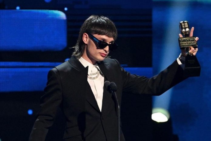 Singer Peso Pluma on stage with a mullet, a black jacket and dark glasses.