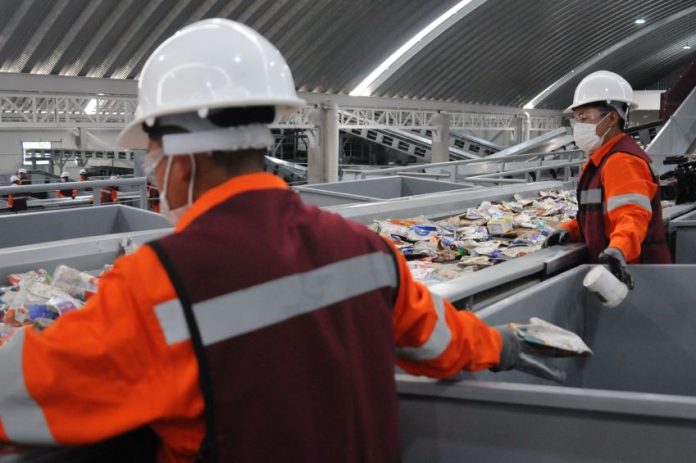 Two workers sort recycling off a conveyor belt