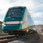 A teal train leaves a station