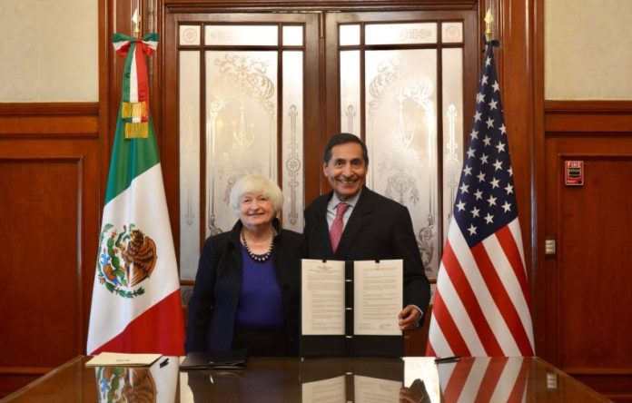 Yellen and Ramírez hold a document while standing next to Mexican and U.S. flags in a conference room.