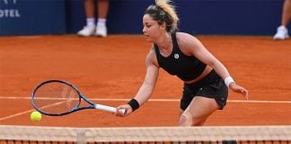 A woman in black tennis gear runs across the court towards the ball.
