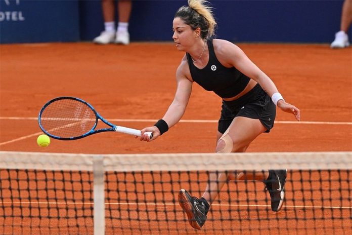 A woman in black tennis gear runs across the court towards the ball.
