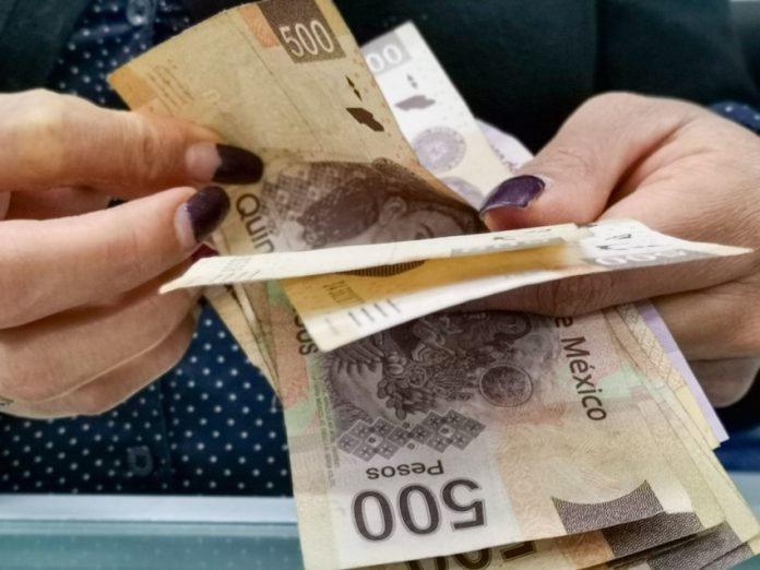 Hands flip through a stack of 500-peso bills