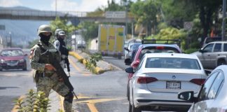 Armed security forces stand guard next to a busy highway