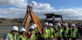 A group of politicians in hard hats pose with shovels at a construction site