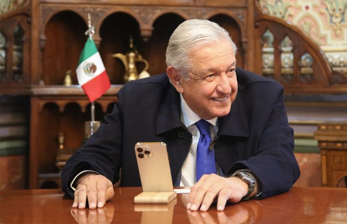 López Obrador sits in front of a smartphone on a phone stand, smiling