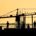 A silhouetted photo of a construction crane and workers