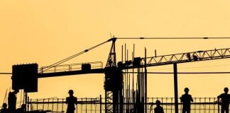 A silhouetted photo of a construction crane and workers
