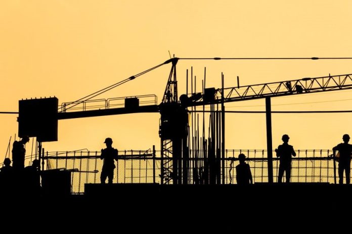 A silhouetted photo of a construction crane and workers