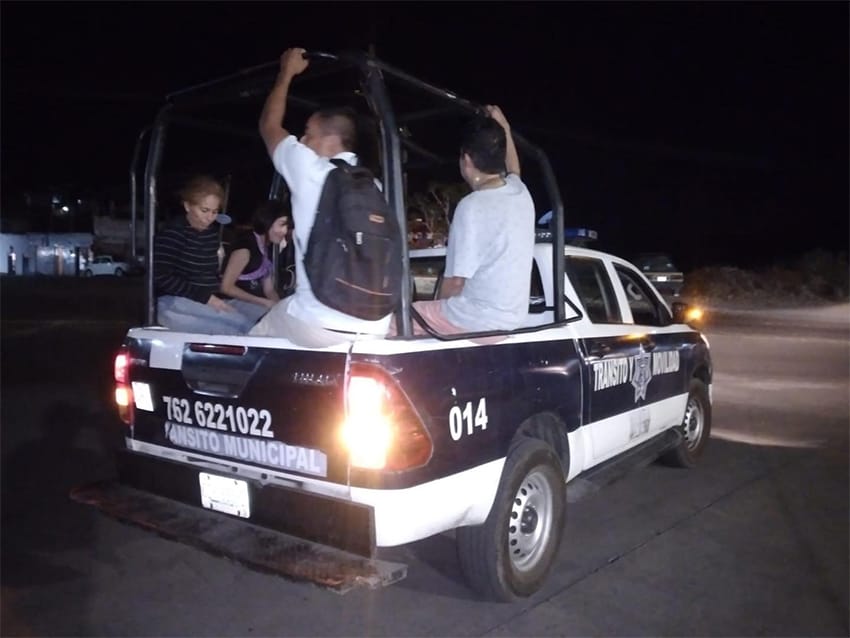 Men and women ride in the back of a pickup police truck.