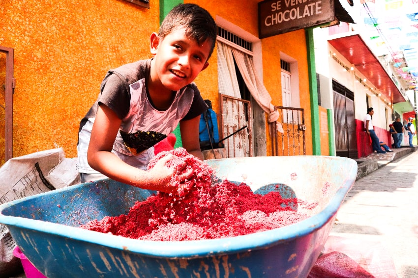 A young boy smiles while preparing colored sawdust for a religious event