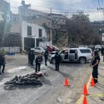 Police stand guard around the scene of a crash, with a damaged car and motorcycle