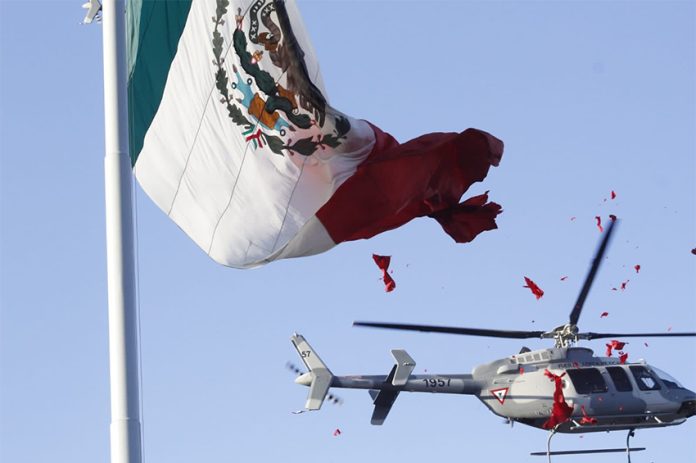 A helicopter blade catches the edge of a Mexican flag, tearing it to pieces